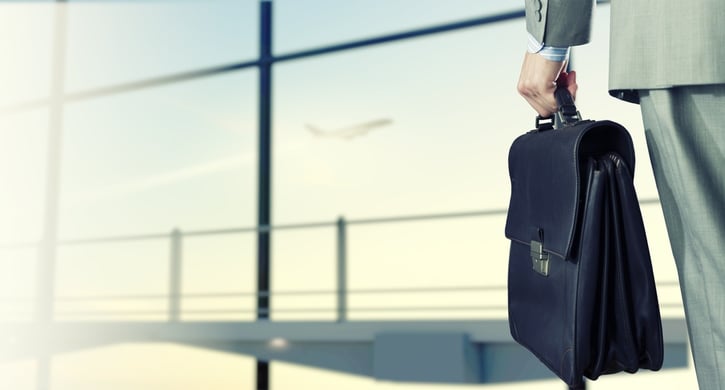 Back view of businessman at airport with suitcase in hand.jpeg