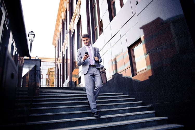 Happy businessman walking on the stairs and using smartphone outdoors