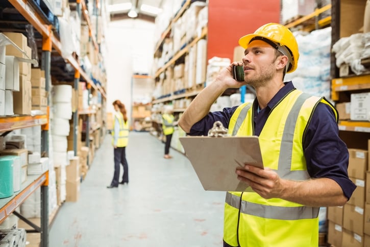 Warehouse worker talking on the phone holding clipboard in a large warehouse.jpeg